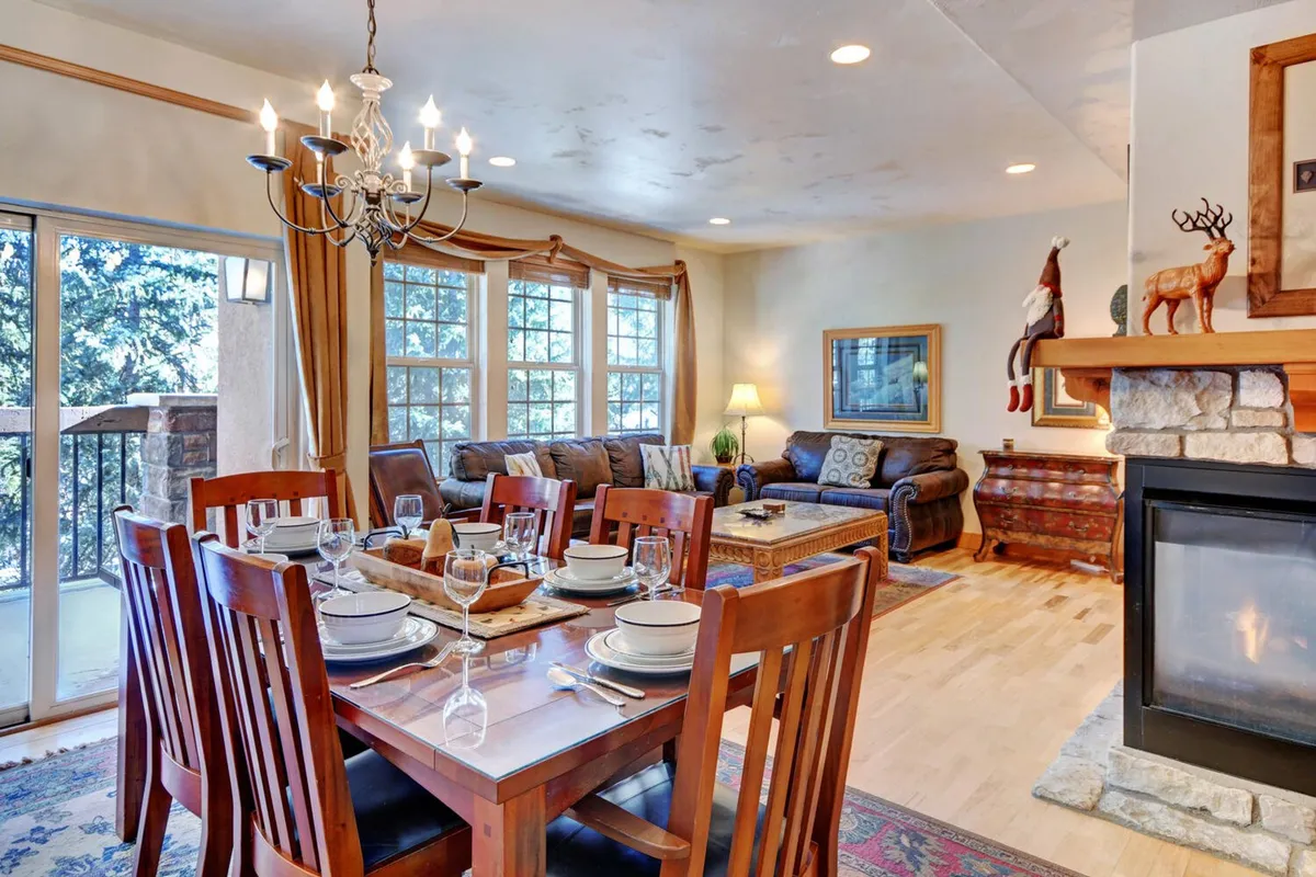 A spacious open-concept area connects a dining table, cozy sofa, and fireplace. Large windows let in abundant sunlight, and the space is clearly designed for both dining and relaxing after a day of adventure. The cohesive layout supports communal gatherings and conversations.