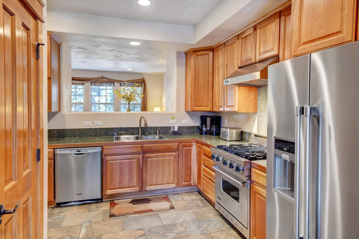 A cozy and inviting kitchen space is depicted, with stainless steel appliances, granite countertops, wooden cabinets, and a window with drapes. The kitchen looks ready for hosting dinner parties or preparing family meals, offering a comfortable yet upscale environment for aspiring chefs.