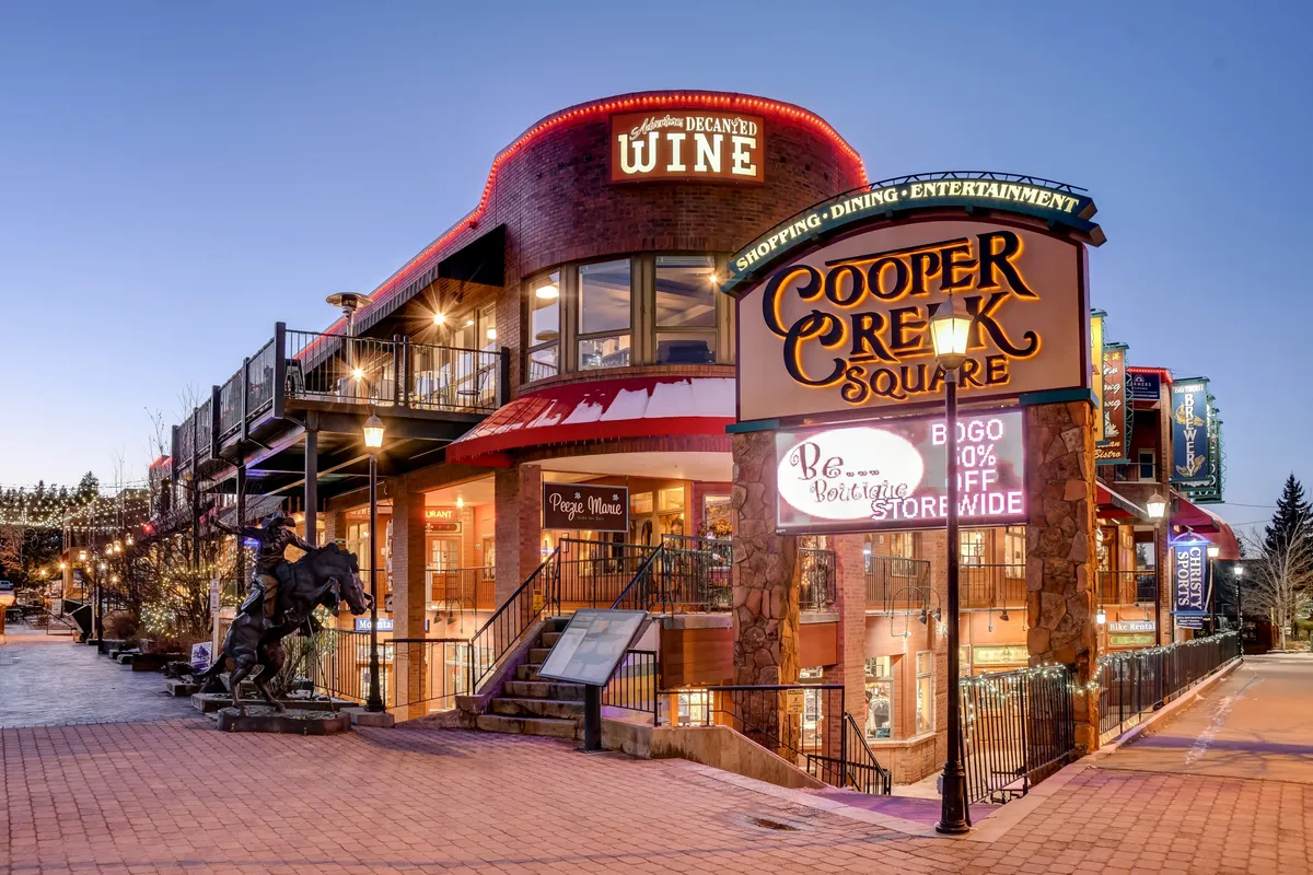 An exterior shot of Cooper Creek Square, showcasing festive lighting, signage for shops and restaurants, and a lively public atmosphere. The scene evokes the vibrancy and community feel of local attractions near the property.