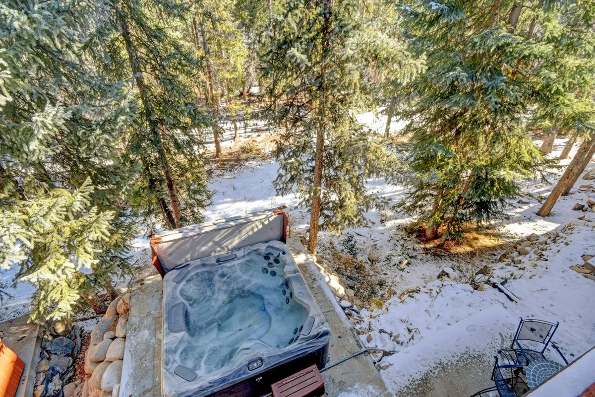 An inviting outdoor hot tub is surrounded by snow-covered ground and tall trees, creating a serene winter setting. The steam rising from the water contrasts beautifully with the crisp white snow, while the secluded location offers a private retreat to enjoy the natural landscape.