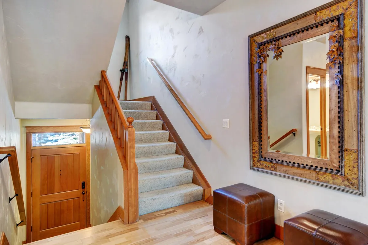 This image captures the inviting entryway of the townhome, featuring a staircase, decorative mirror, front door, and footstools. Natural light brightens the space, and the design hints at a welcoming transition from the outdoors to the comforts of the home.