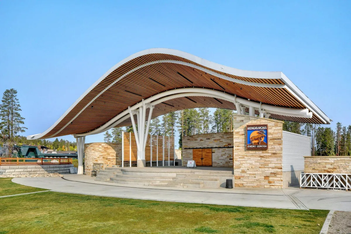 An outdoor amphitheater with a curved roof structure and open stage area, surrounded by stone walls. The space is set up for community events and live performances, conveying an energetic, celebratory mood perfect for gatherings and festivals.