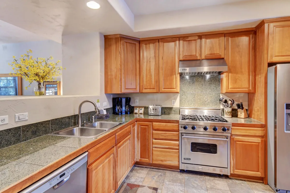 The chef-inspired kitchen features wooden cabinets, stainless steel appliances, granite countertops, and a decorative vase. The setup is both functional and stylish—ideal for group meals or sharing coffee as described in the section.