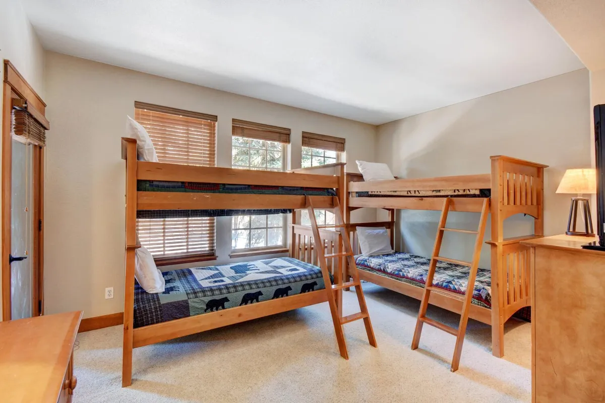 A bright and cheerful bunk room with sturdy wooden bunk beds, a window letting in natural light, and a matching wooden dresser. The space feels playful yet practical, evoking the excitement of sleepovers and group stays.